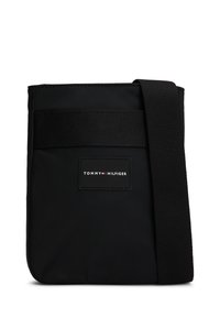 Schwarze Tommy Hilfiger Umhängetasche mit verstellbarem Riemen und Markenlogo-Patch auf der Vorderseite.