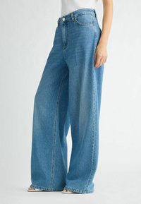 Jeans a gamba larga in denim azzurro chiaro con vita alta, dotati di un classico design a cinque tasche e cuciture visibili lungo le cuciture.