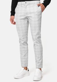 Lysegrå mønstrede tapered bukser lavet af et blødt stof, parret med hvide sneakers og en sort langærmet skjorte.