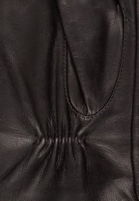 Schwarzes Leder mit glatter Textur, das über geraffte Details und einen dezenten Glanz verfügt. Die Oberfläche zeigt feine Nähte und geschwungene Linien.