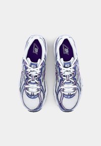 Sapatos atléticos brancos com detalhes em púrpura, parte superior em malha, sola grossa e detalhes de design intrincados. Atilhos e logótipo em destaque.