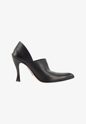 Zapato de tacón alto de cuero negro con puntera puntiaguda, parte trasera cerrada y tacón de aguja curvado sobre fondo blanco.