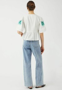 Hvid peplum-top med korte puffærmer og grøn blomsterbroderi, parret med lyseblå bredbensjeans. Glat stoftekstur.