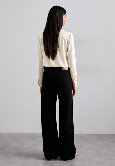 Cream blouse with long sleeves, paired with high-waisted, wide-leg black jeans. Smooth texture and subtle stitching details visible.