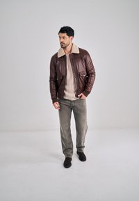 Hnědá kožená bomber bunda s krémovým límcem z beránkové vlny, svetr s úpletem ve tvaru kabelu a šedé kordurové kalhoty. Černé semišové boty doplňují vzhled.