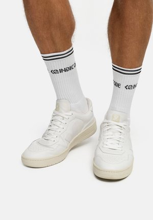 Hvide lædersneakers med perforeret tåboks og lysfarvet sål, kombineret med hvide sokker med sorte striber og logotekst.