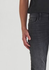 Vaqueros de denim gris oscuro con un diseño ajustado, que cuentan con un bolsillo frontal y sutiles detalles de costura. Textura suave con mínimo hardware.