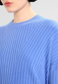 Niebieski sweter w prążki z poziomymi i ukośnymi wzorami teksturowymi, okrągłym dekoltem i miękkim materiałem dzianinowym. Zbliżenie na detale tkaniny.