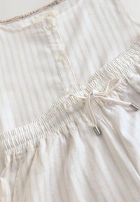 Robe légère en tissu crème avec des rayures verticales beiges, dotée de boutons au niveau du cou, d'une taille élastique et de détails à cordon ajustable.