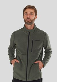 Fleece jacket in dark green with a high collar and zip front. Features two side pockets and a zippered chest pocket with black detailing.