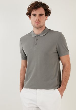 Polo gri dintr-un material texturat, cu un guler clasic, mâneci scurte și un sistem de închidere cu trei nasturi, asociat cu pantaloni deschiși la culoare.