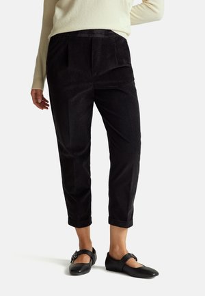 Zwarte corduroy broek met een rechte snit, voorzien van voorplooien en opgerolde boorden, gecombineerd met zwarte schoenen. Textuurstof, neutrale stijl.