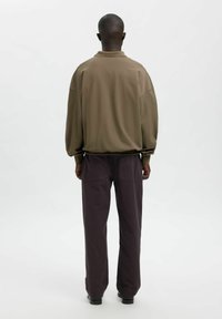 Olīvekļļains zaļš pārizmēra džemperis ar apaļu kaklu un nolaižamām pleciem, kombinēts ar tumši violeta plašu kāju bikšu, kurās ir aizmugurējās kabatas.