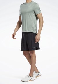 Ljusgrön idrottströja med korta ärmar, kombinerad med svarta shorts. Modellen har vita sneakers med en texturerad yta och svarta detaljer.
