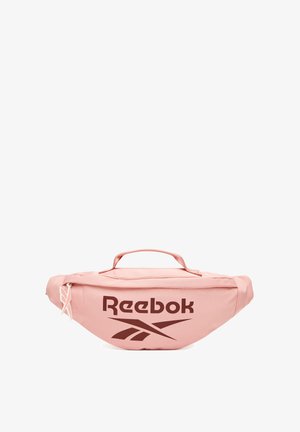 Riñonera Reebok de color rosa claro con logo marrón oscuro, cierre de cremallera y asa superior sobre un fondo blanco.