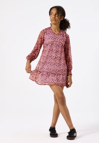 Vestido con estampado floral en una tela ligera y transparente. Presenta un escote en V, mangas largas con volantes y un dobladillo escalonado en tonos de rosa y púrpura.