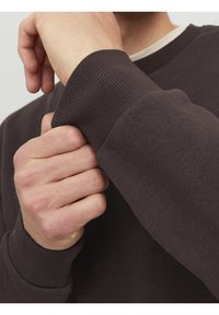 Felpa marrone scuro con polsini a costine, in tessuto di cotone, caratterizzata da un colletto a strati con una camicia interna di colore chiaro visibile sotto.