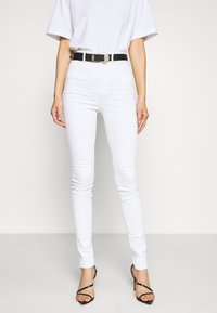 Jeans de mezclilla blanca con corte ajustado, combinados con un cinturón negro con una hebilla metálica decorativa, complementados con tacones negros con tiras.