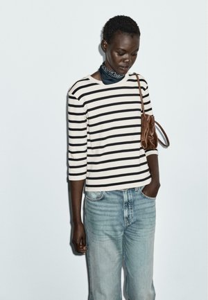 Striped long-sleeve top in cream and black, paired with light blue jeans. Accessorized with a brown handbag and a blue scarf around the neck.