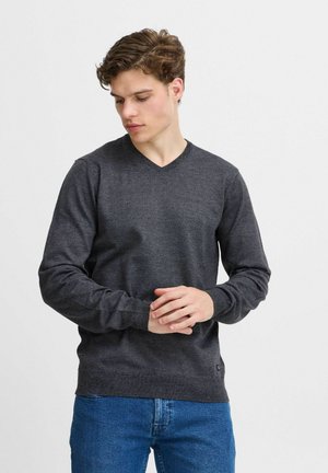 Mørk grå V-hals genser, strikket tekstur, lange ermer, ribbestrikkede mansjetter og hem, båret med blå jeans. Subtilt design, ingen synlige logoer.