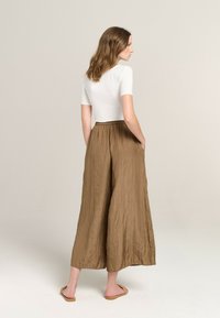 Brown, crinkled wide-leg pants with an elastic waistband and pockets, paired with a fitted white top, viewed from the back.