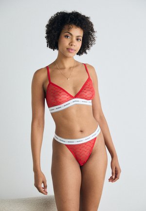Set di lingerie rossa in pizzo composto da un bralette triangolare e un perizoma, con una fascia elastica bianca con marchio. Il tessuto presenta un motivo sottile.