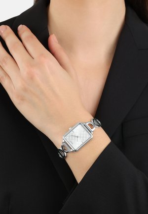 Silberne Uhr mit quadratischem Ziffernblatt und gemustertem weißen Ziffernblatt, gesichert mit einem schwarzen Armband mit silbernen Akzenten und Gliedern.