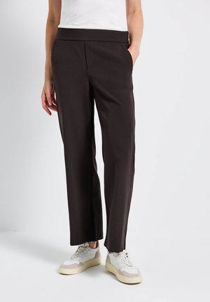 Black, high-waisted trousers with a smooth texture, wide legs, and two side pockets; paired with white and beige sneakers.
