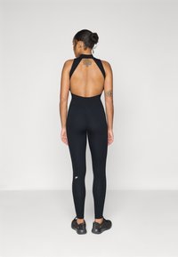 Body atletico nero con schiena scoperta, design aderente e gambe di taglio alto. Presenta cuciture piatte e un piccolo logo bianco sulla gamba sinistra.