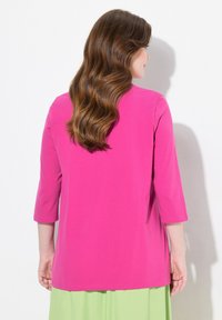 Fuchsia roze top met driekwartmouwen gemaakt van zachte, gladde stof met een ontspannen pasvorm, gecombineerd met een groene rok.