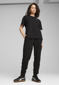 Camiseta negra de manga corta, con un pequeño logo. Combinada con pantalones de chándal negros y zapatillas negras con acentos grises.