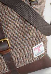 Textured brown and multicolored Harris Tweed bag with a brown leather base. Features a fabric strap and logo label with care instructions.