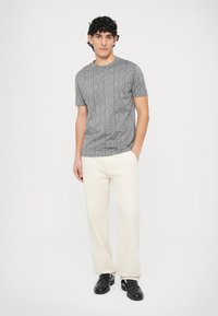 Szara koszulka z krótkim rękawem o delikatnej, wzorzystej fakturze, zestawiona z białymi spodniami i czarnymi wsuwanymi butami. Prosty i nowoczesny design.