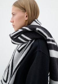 Sciarpa di lana a righe bianche e nere avvolta attorno al collo, con strisce audaci e texture morbida, sovrapposta a un indumento nero.