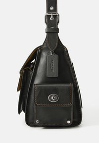 Black leather bag with metal accents, a front pocket, and contrasting brown stitching. Features a shoulder strap and brand tag detail.