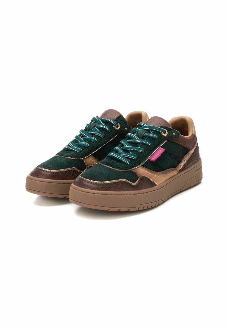 Une paire de baskets basses en daim vert, avec des accents en cuir marron, des semelles en gomme, des lacets verts et blancs, et une petite étiquette rose sur le côté.