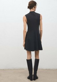 Black sleeveless dress with a fitted bodice and flared skirt, paired with knee-high black boots and smooth textures, set against a plain background.
