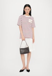 T-shirt rayé avec une poche, associé à un short blanc, tenant un sac à main en cuir noir. Des mules pointues noires complètent la tenue.
