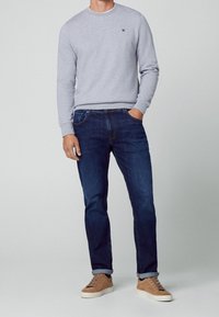Grå crewneck-sweatshirt med lange ærmer, kombineret med mørkeblå jeans og beige sneakers. Sweatshirten har et lille logo på brystet.