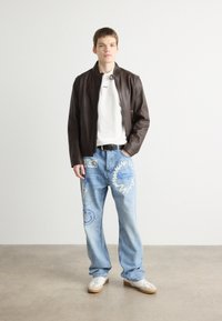 Brown leather jacket over a white t-shirt, light blue jeans with blue graphic designs, and white sneakers with beige accents.