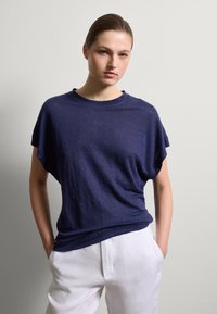 Marineblaues, locker sitzendes T-Shirt mit kurzen Ärmeln und rundem Ausschnitt, aus einem weichen, strukturierten Stoff, kombiniert mit weißen Leinenhosen.