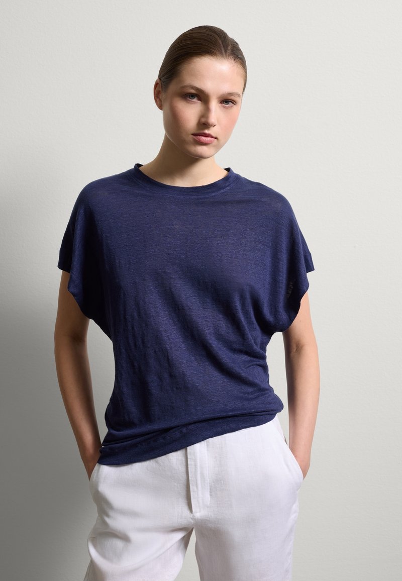 Marineblaues, locker sitzendes T-Shirt mit kurzen Ärmeln und rundem Ausschnitt, aus einem weichen, strukturierten Stoff, kombiniert mit weißen Leinenhosen.