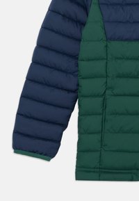 Navy blue sleeve and dark green quilted section of a padded jacket with horizontal stitching and a side pocket visible.