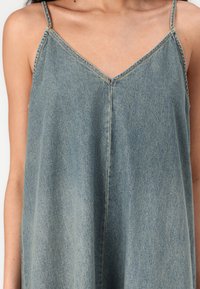 Denim slipkjole med V-hals, tynne stropper og digg passform. Har en lys blå vask og subtilt falmet tekstur.
