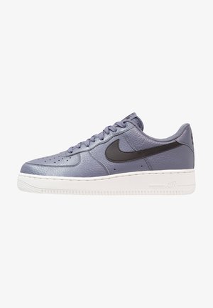 Tenisky Nike Air Force 1 v světle fialkové kůži, s černým swooshem, perforovanou špičkou a bílou gumovou podrážkou.