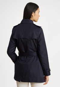 Námornícky trenčkot s opaskom v páse, zapínanými lištami na ramenách a s rozparkom na chrbte. Vyrobený z hladkej, odolnej látky s mierne strihaným strihom.