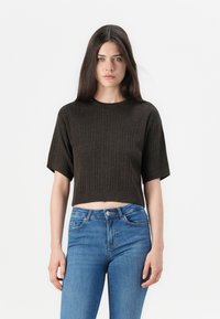 Brun kort stickad tröja med korta ärmar och ribbad textur, tillsammans med högmidjade blå jeans.
