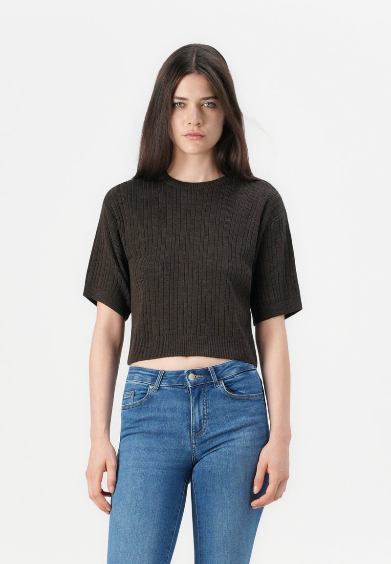 Brun kort stickad tröja med korta ärmar och ribbad textur, tillsammans med högmidjade blå jeans.