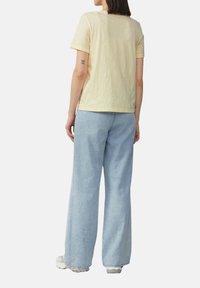 T-shirt en coton jaune avec une coupe décontractée, des manches courtes et un col rond, associé à un jean large bleu clair et des baskets blanches.