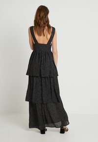 Abito maxi nero a strati con schiena bassa, caratterizzato da piccole pois bianche. Realizzato in tessuto leggero con una silhouette fluida.
